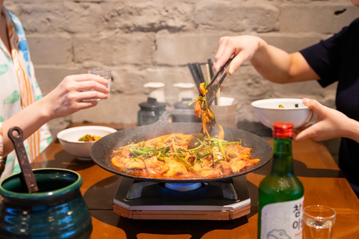 タッカンマリ食べ放題の「晴レ時々タッカンマリ食堂」に山盛りのセリを豪快に崩して味わう新感覚の鉄板鍋”旨辛タッコギ鉄板鍋”が夏の看板メニューとして新登場！7月24日から。